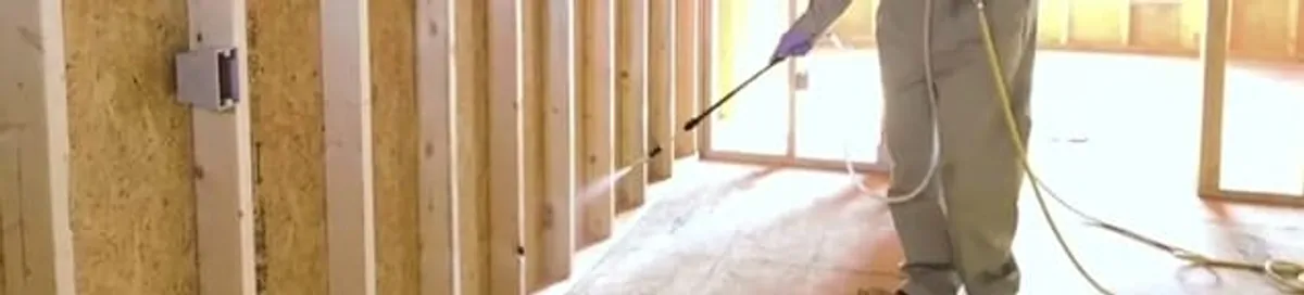 Termite treatment technician applying spray along framing and unfinished walls in Ann Arbor, MI